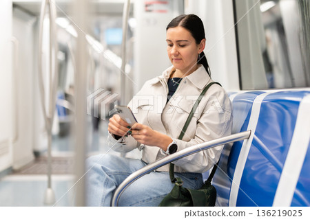 Girl in modern subway car scrolling smartphone 136219025