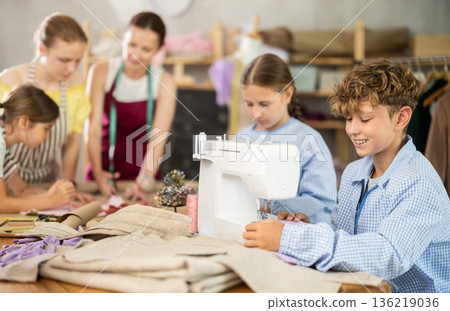 Teen boy child sews during practical lesson at school of young fashion designers Teen boy child sews during practical lesson at school of young fashion designers 136219036