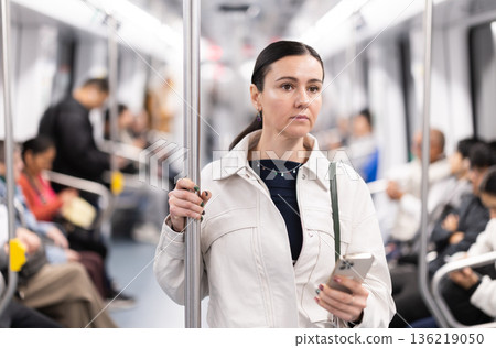Woman with phone stand in metro carriage. 136219050
