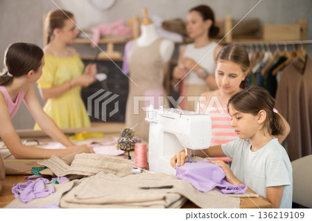 Girl sews on a sewing machine. Boy watches and learns Girl sews on a sewing machine. Boy watches and learns 136219109