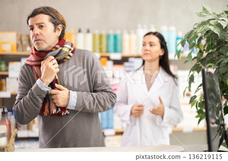 Man with sore throat and cough choosing pills with help from pharmacist 136219115