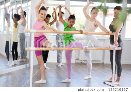 Group of teenage girls stretching at ballet barre in beginner class Group of teenage girls stretching at ballet barre in beginner class 136219117