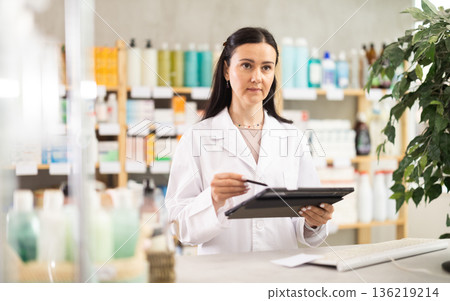 Middle-aged female pharmacist restocking with tablet in drugstore Middle-aged female pharmacist restocking with tablet in drugstore 136219214