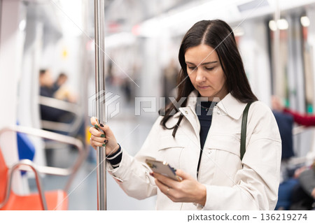 Woman stand in metro carriage, scrolls through social media feed 136219274