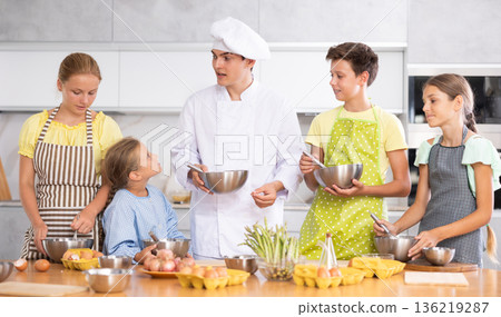 Friendly young chef running culinary courses for group of children Friendly young chef running culinary courses for group of children 136219287