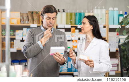 Man chooses pills in modern pharmacy. Female pharmacist helps with choosing medicine Man chooses pills in modern pharmacy. Female pharmacist helps with choosing medicine 136219296
