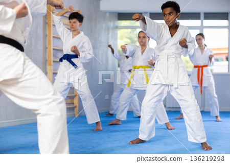 Group of preteen children of different nationalities in kimono trying new martial moves at gym 136219298