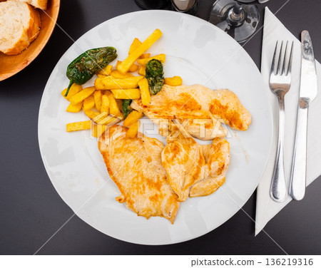 Tender meat of baked chicken breast is garnished with French fry potato 136219316