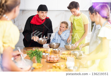 Cooking class, culinary, food and people concept - happy group of children and male chef cook cooking in modern kitchen Cooking class, culinary, food and people concept - happy group of children and male chef cook cooking in modern kitchen 136219351