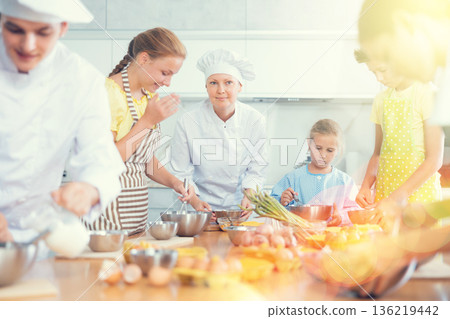 Young guy and adult woman cook teaches group of children to cook Young guy and adult woman cook teaches group of children to cook 136219442