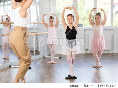 Girl students of choreographic school look at woman teacher and repeat movements after her Girl students of choreographic school look at woman teacher and repeat movements after her 136219452