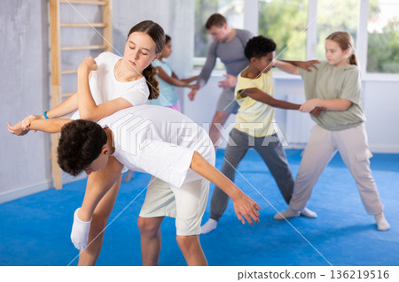 Girls and boys practicing in pair self defence movements with male trainer supervision Girls and boys practicing in pair self defence movements with male trainer supervision 136219516