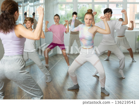 Young girls and boys repeat the movements of dance teacher, training in spacious studio Young girls and boys repeat the movements of dance teacher, training in spacious studio 136219541