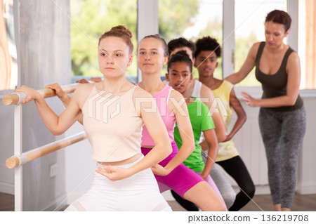 Teenage girl learning demi plie at barre with group of ballet students 136219708