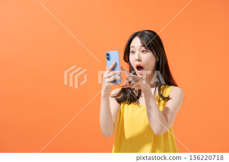 A woman with a surprised expression holding a smartphone 136220718