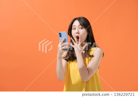 A woman with a surprised expression holding a smartphone 136220721