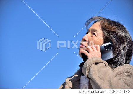 Senior woman talking on a mobile phone under the blue sky Senior woman talking on a mobile phone under the blue sky 136221380