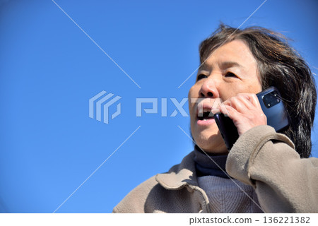 Senior woman talking on a mobile phone under the blue sky Senior woman talking on a mobile phone under the blue sky 136221382