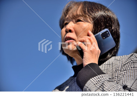 Senior woman talking on a mobile phone under the blue sky Senior woman talking on a mobile phone under the blue sky 136221441