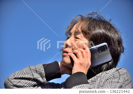 Senior woman talking on a mobile phone under the blue sky Senior woman talking on a mobile phone under the blue sky 136221442