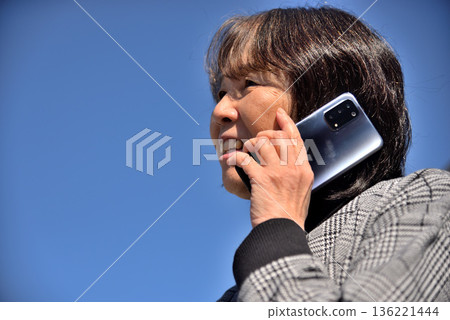 Senior woman talking on a mobile phone under the blue sky 136221444