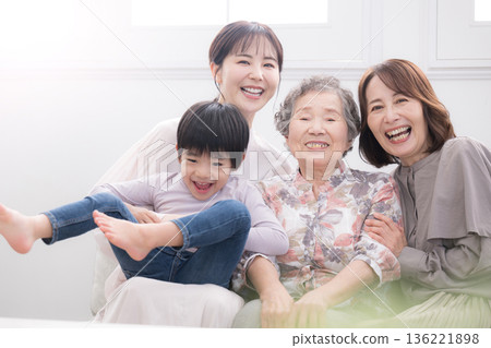 A four-generation family: grandmother, mother, and child (great-grandchild) smiling and embracing each other in a beautiful backlit room; a happy scene of parents and children looking at the camera A four-generation family: grandmother, mother, and child (great-grandchild) smiling and embracing each other in a beautiful backlit room; a happy scene of parents and children looking at the camera 136221898