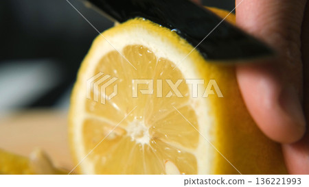 Macro close-up of slicing lemon with knife on board, showing juicy texture and color. Healthy vitamin and freshness concept Macro close-up of slicing lemon with knife on board, showing juicy texture and color. Healthy vitamin and freshness concept 136221993