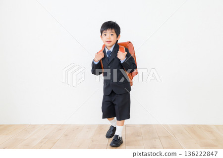 A boy in a suit carrying a school bag 136222847