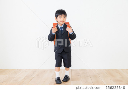 A boy in a suit carrying a school bag 136222848