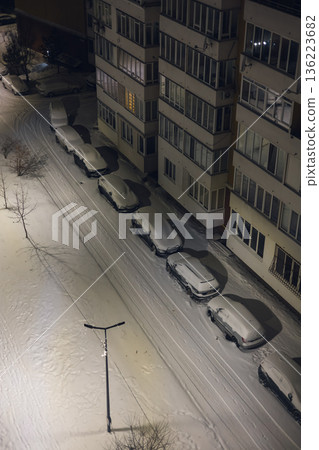 Lviv Ukraine 01.01.26 Snow covers cars on a quiet street near an apartment building at night Lviv Ukraine 01.01.26 Snow covers cars on a quiet street near an apartment building at night 136223682