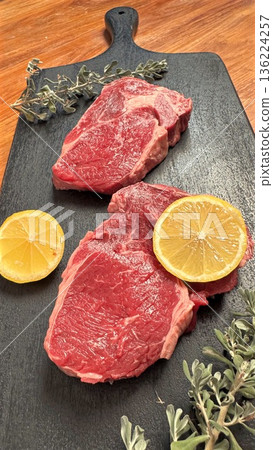 Homestyle Cooking Scene Featuring Raw Beef And Aromatic Herbs On Wood, Country Style Kitchen Setting Showcasing Uncooked Steaks Ornamented With Herbs And Warm Wooden Backgrounds 136224257