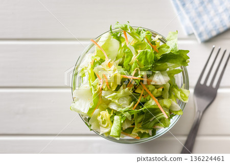 Mix of fresh green salad with carrot in bowl on white table. Top view. Mix of fresh green salad with carrot in bowl on white table. Top view. 136224461