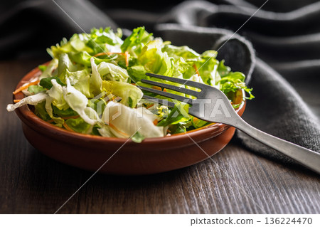 Mix of fresh green salad with carrot in bowl on wooden table. 136224470