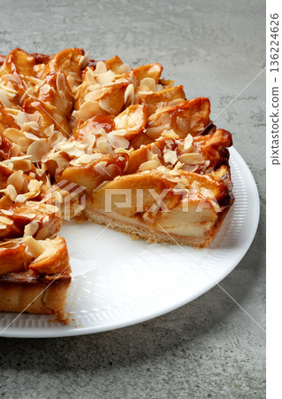 Delicious apple tart with almond topping on a white plate in a kitchen setting Delicious apple tart with almond topping on a white plate in a kitchen setting 136224626