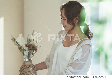 A stylish Asian woman arranging dried flowers in a vase 136225055