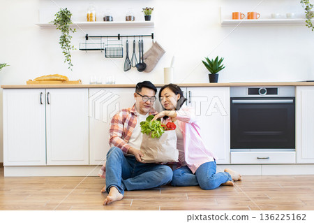 A happy couple unpacks a bag of fresh groceries in their bright, modern kitchen A happy couple unpacks a bag of fresh groceries in their bright, modern kitchen 136225162