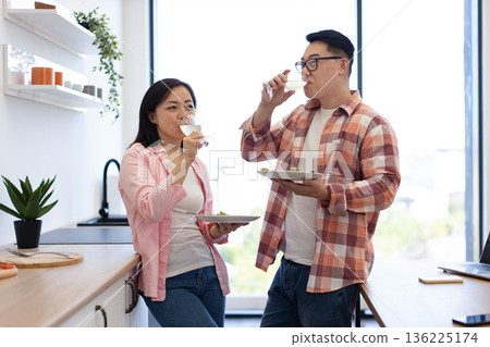 An Asian couple enjoys a meal and drinks wine together in their modern kitchen An Asian couple enjoys a meal and drinks wine together in their modern kitchen 136225174
