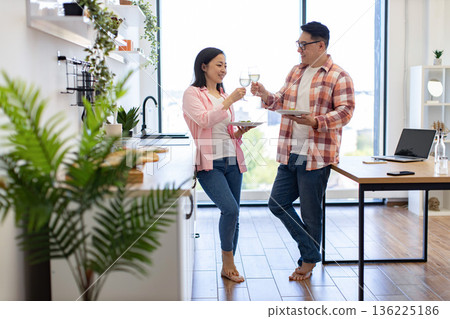 An Asian couple enjoys a meal and drinks wine together in their modern kitchen An Asian couple enjoys a meal and drinks wine together in their modern kitchen 136225186