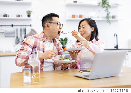 An Asian couple enjoys a healthy meal together in their kitchen, showing love and connection 136225198