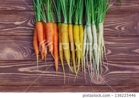 Yellow, orange and white carrots on the brown wooden table. 136225446