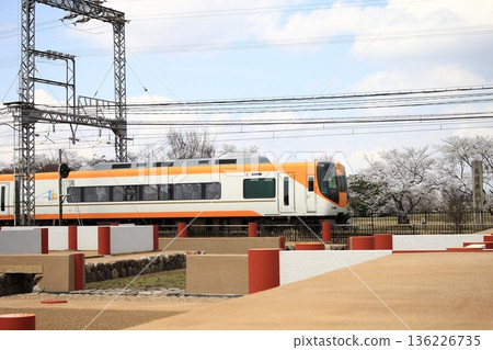 A limited express train on the Kintetsu Nara Line runs alongside the cherry blossom trees in full bloom and the restored ruins at the Heijo Palace Ruins, a World Heritage Site. 136226735