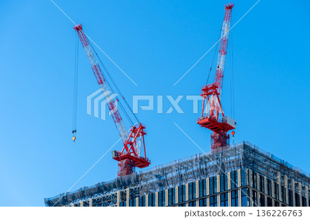 在湛藍的天空下，一棟紅色起重機高聳於一棟在建建築之上。 136226763