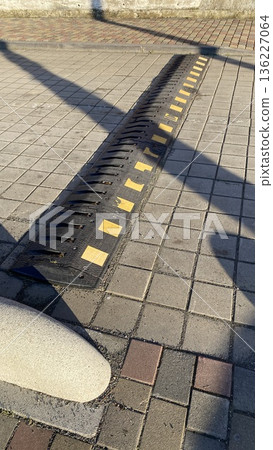 Black rubber speed bump with yellow reflective markings embedded in a pedestrian sidewalk to slow traffic in urban areas. Black rubber speed bump with yellow reflective markings embedded in a pedestrian sidewalk to slow traffic in urban areas. 136227064