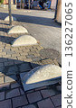 Rounded concrete bollards are aligned along a paved walkway, serving as barriers to prevent vehicle access on sidewalks.  136227065