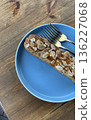 Uncut almond pastry topped with sliced almonds, placed on a vibrant blue plate with two forks beside it.  136227068
