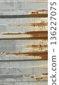 Close-up of a gray corrugated metal wall with brown rust lines and aged texture, ideal for industrial backgrounds.  136227075