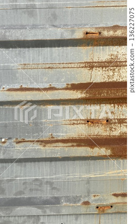 Close-up of a gray corrugated metal wall with brown rust lines and aged texture, ideal for industrial backgrounds. Close-up of a gray corrugated metal wall with brown rust lines and aged texture, ideal for industrial backgrounds. 136227075