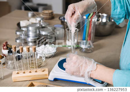 Hands in gloves pour pink minerals from plastic bag into glass test tube on digital scale in apothecary setting. magnesium flakes DIY, transdermal recovery, muscle soak science, bioavailable salts. Hands in gloves pour pink minerals from plastic bag into glass test tube on digital scale in apothecary setting. magnesium flakes DIY, transdermal recovery, muscle soak science, bioavailable salts. 136227953