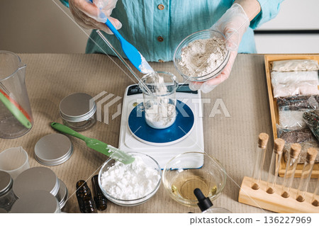 Hands holding small glass bowl pour powder into beaker positioned on digital scale. raw beauty ingredients, skincare transparency, minimalist formulation, natural cosmetic components. Hands holding small glass bowl pour powder into beaker positioned on digital scale. raw beauty ingredients, skincare transparency, minimalist formulation, natural cosmetic components. 136227969