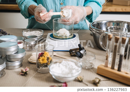 Hands in gloves scoop solid butter from jar into glass beaker on digital scale. raw beauty ingredients, skincare transparency trend, clean beauty formulation, botanical cosmetic actives. Hands in gloves scoop solid butter from jar into glass beaker on digital scale. raw beauty ingredients, skincare transparency trend, clean beauty formulation, botanical cosmetic actives. 136227983